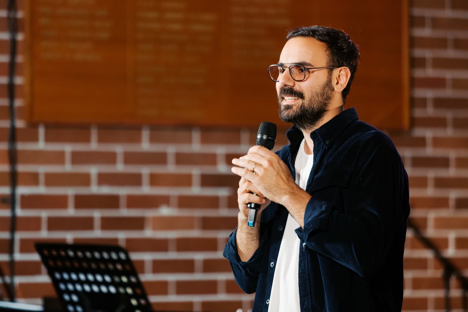 Jade Hajj preaching at Grace City Church in Sydney, holding a microphone in front of a brick wall.